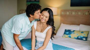 A couple sitting on a bed with a blue quilt and a pillow with a fish pattern.