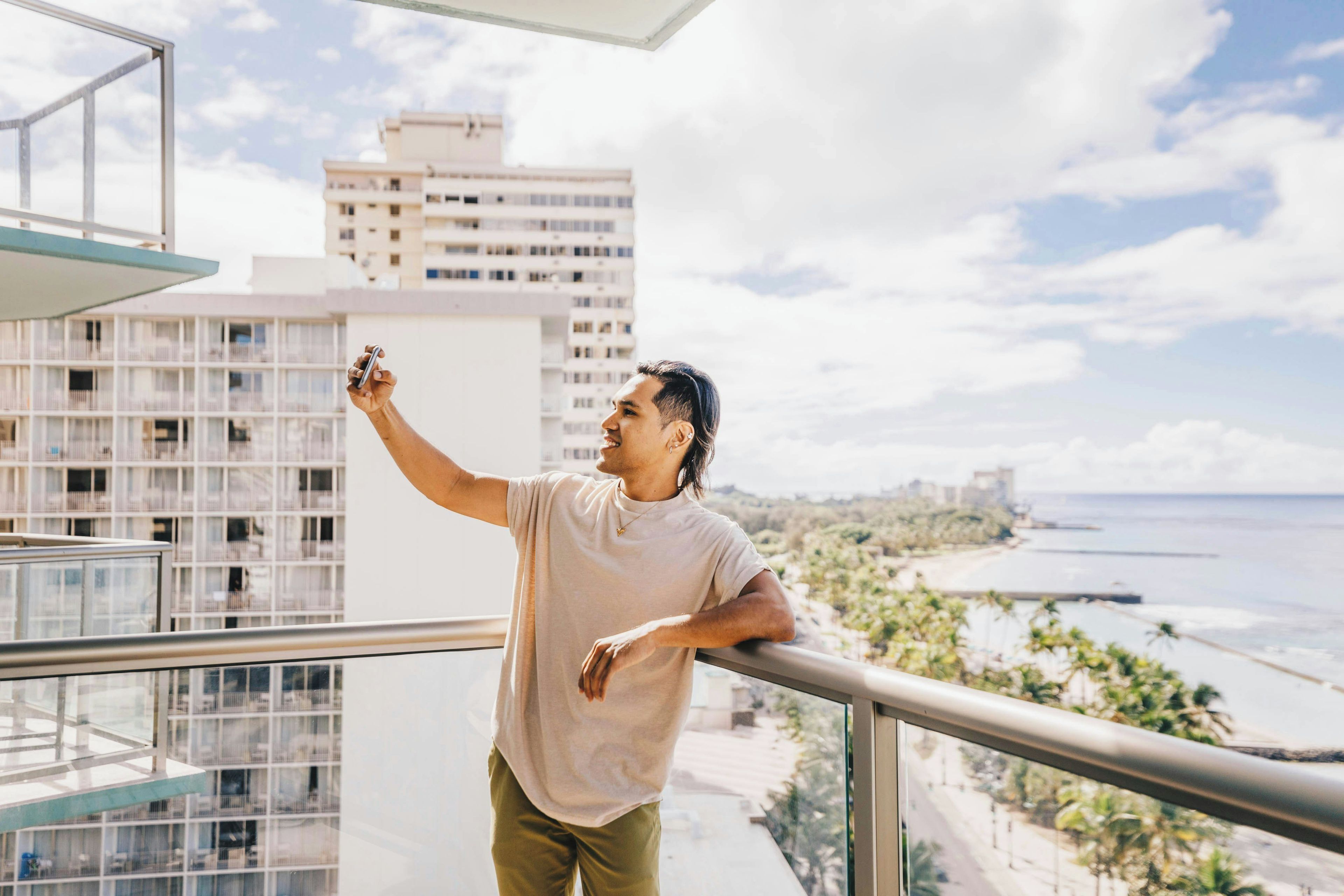 A person standing on a balcony with a view of a beach and buildings in the distance.