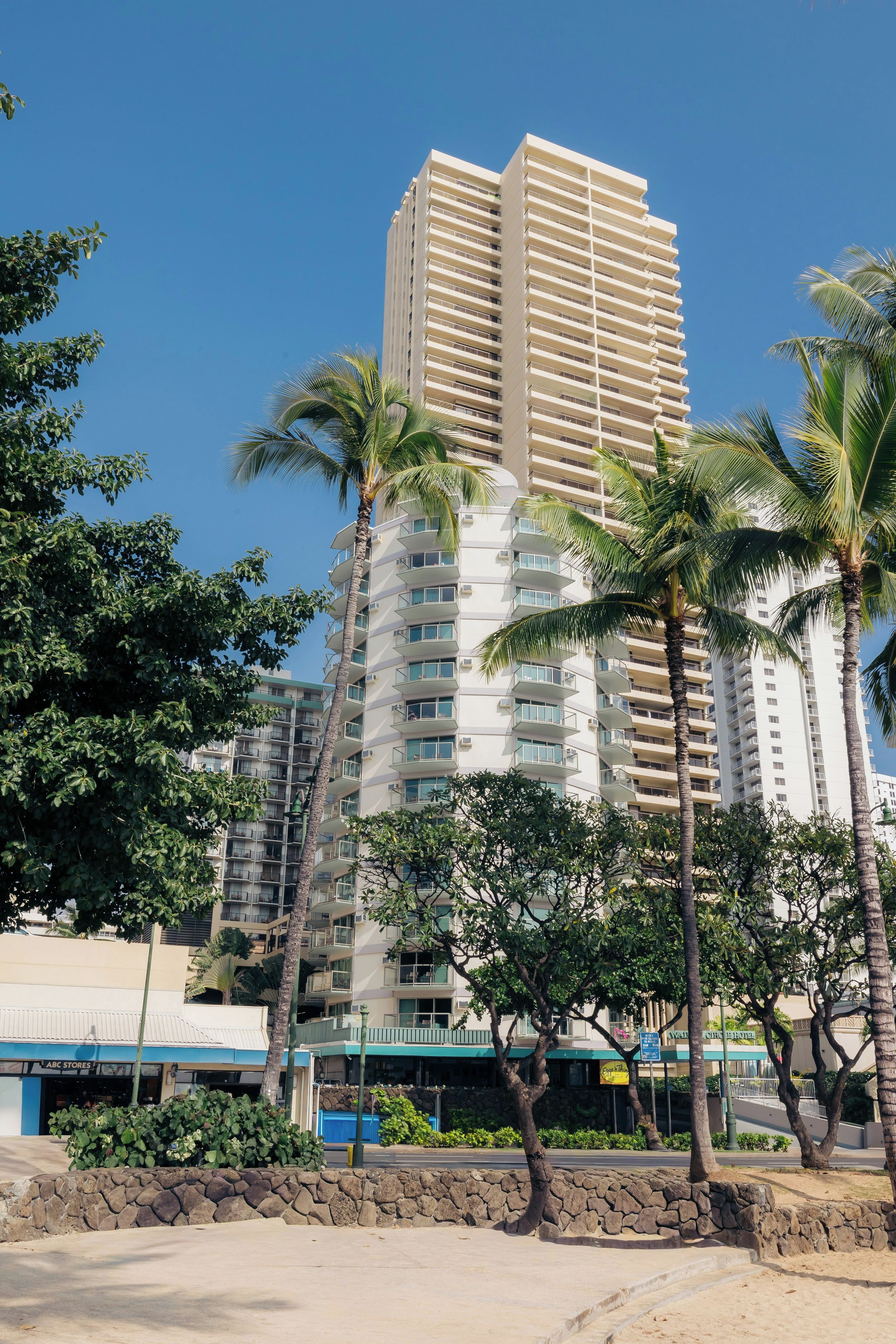 A multi-story hotel with balconies, surrounded by palm trees and a clear blue sky.