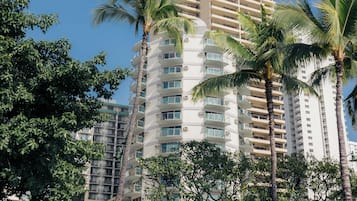 A multi-story hotel with balconies, surrounded by palm trees and a clear blue sky.