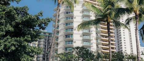 A multi-story hotel with balconies, surrounded by palm trees and a clear blue sky.