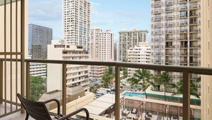 A balcony with a chair, overlooking a pool area with lounge chairs and palm trees. - Waikiki Circle Hotel By Castle (Honolulu)