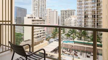 A balcony with a chair, overlooking a pool area with lounge chairs and palm trees.