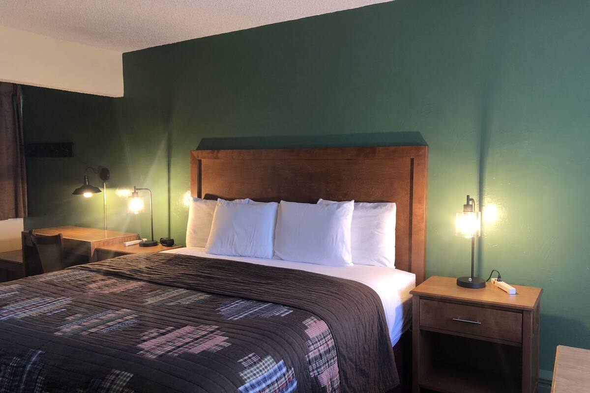 A neatly made bed with a wooden headboard, two bedside lamps, and a small wooden nightstand with a drawer.