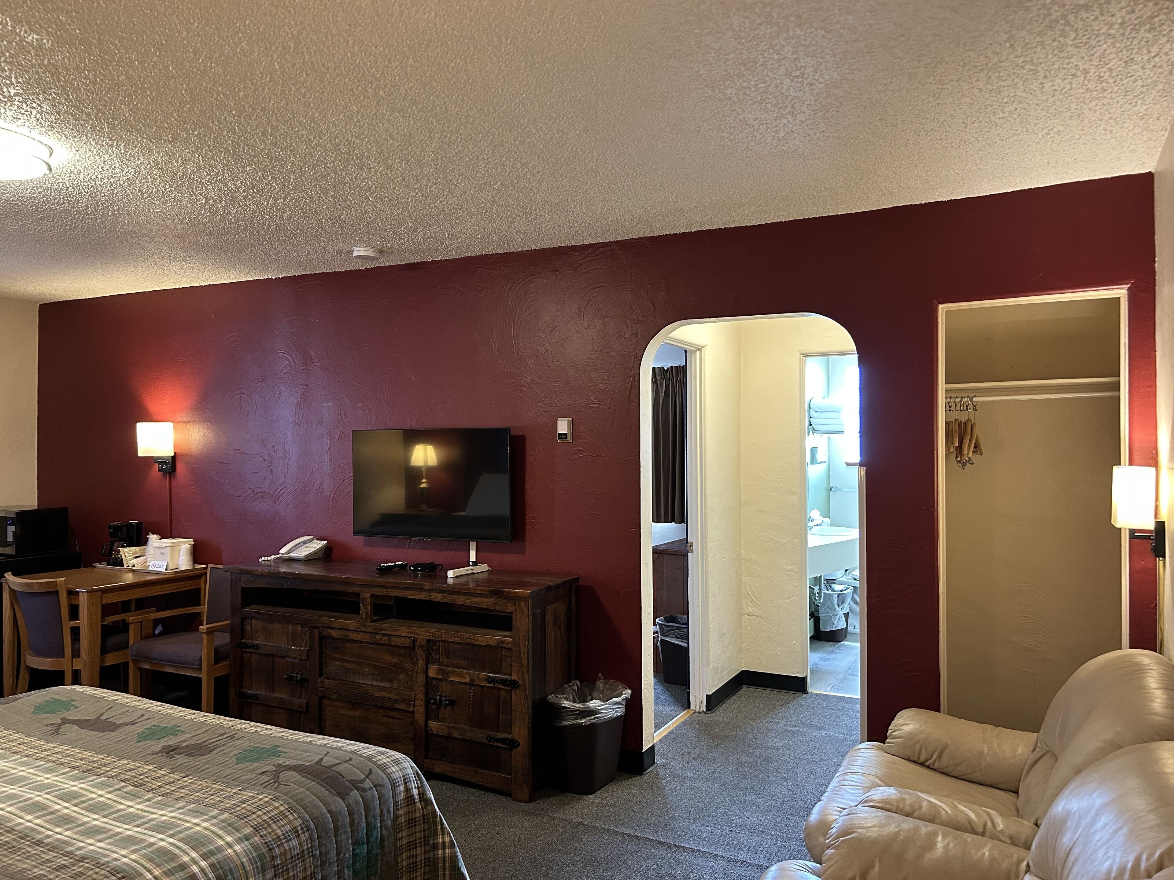 Een hotelkamer met een televisie, een bureau met een lamp, een dressoir, een bed met een geruit sprei en een stoel.