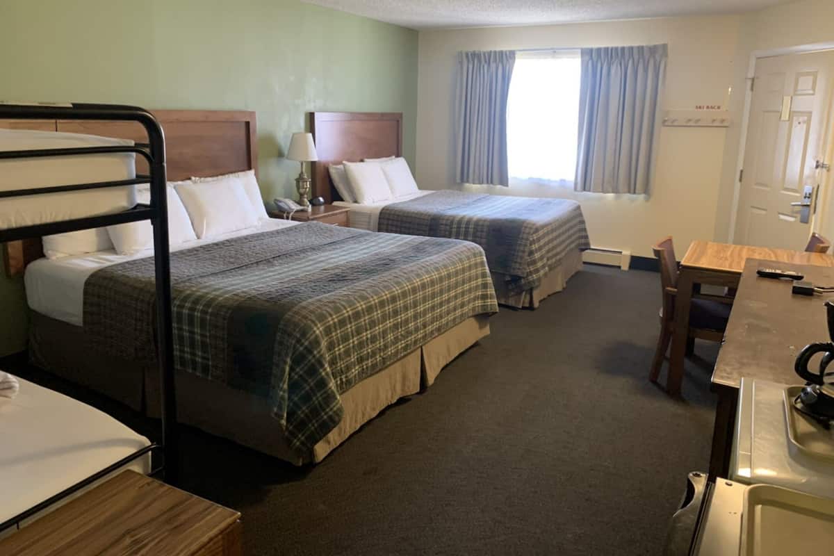 A hotel room with two beds, a desk, a chair, a lamp, and a window with curtains.