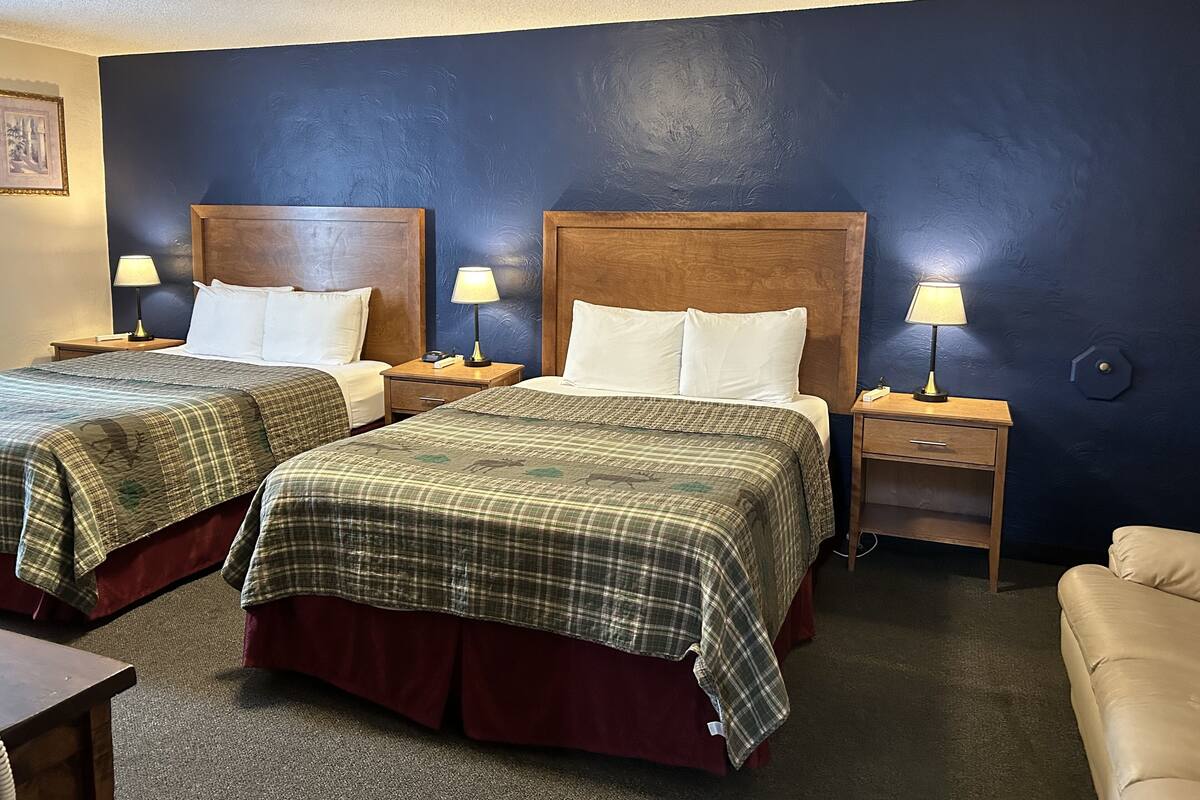 A hotel room with two beds, each with a wooden headboard, a nightstand with a lamp, and a small drawer.