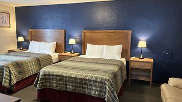 Habitación de hotel con dos camas, cada una con cabecero de madera, mesita de noche con lámpara y un cajón pequeño.