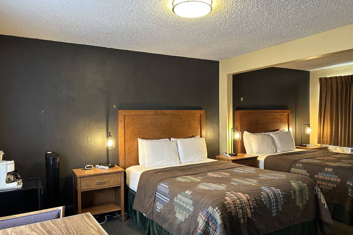 A hotel room with two beds, wooden headboards, bedside lamps, a desk, and a chair.