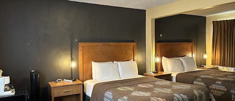 A hotel room with two beds, wooden headboards, bedside lamps, a desk, and a chair.