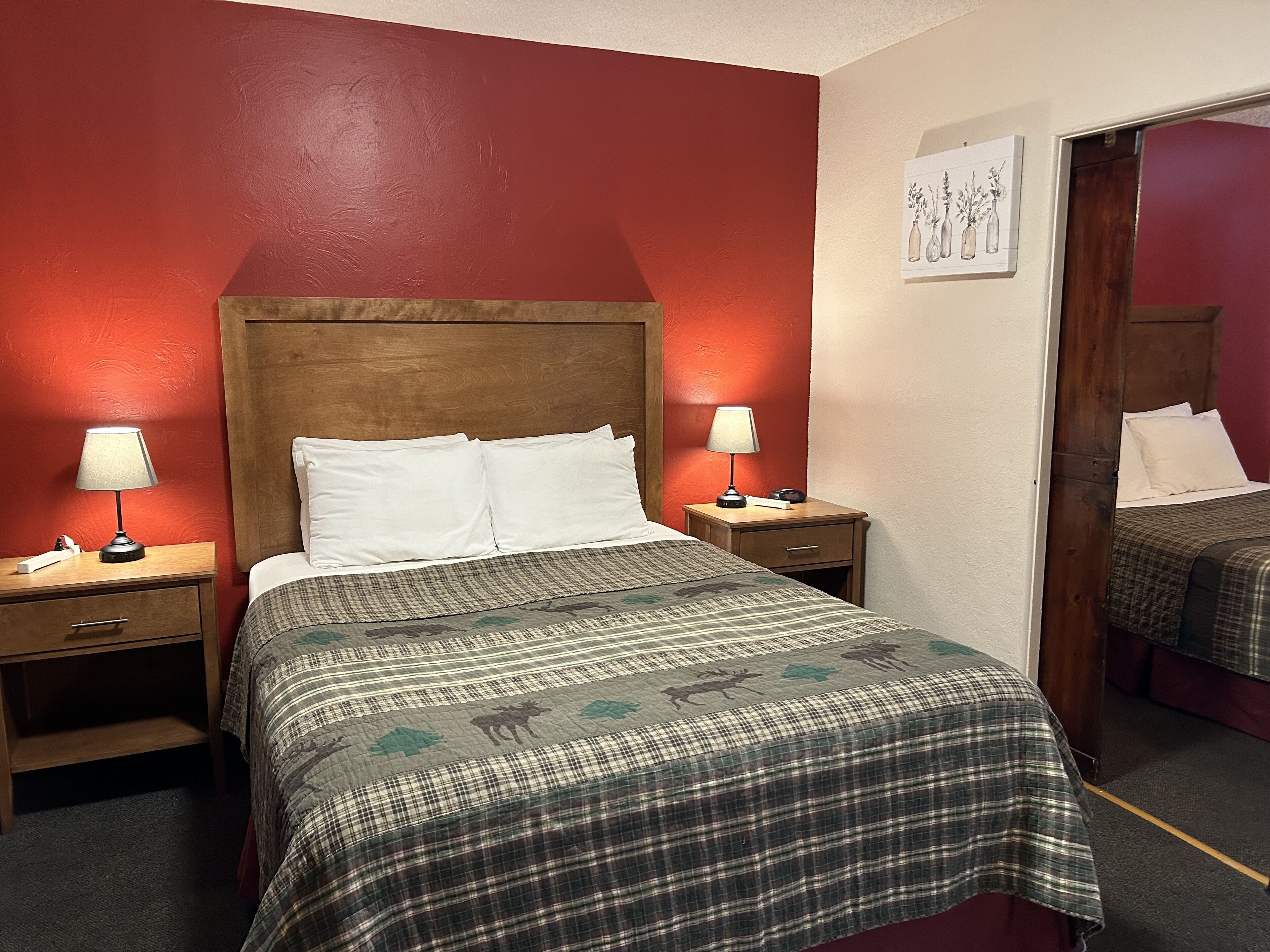 A hotel room with a large bed, two bedside tables, a nightstand, a mirror, and a wall-mounted artwork.