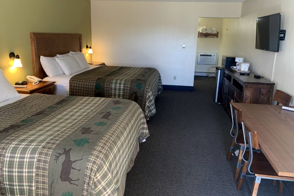 A hotel room with two beds, a desk, a chair, a TV, and a kitchenette.