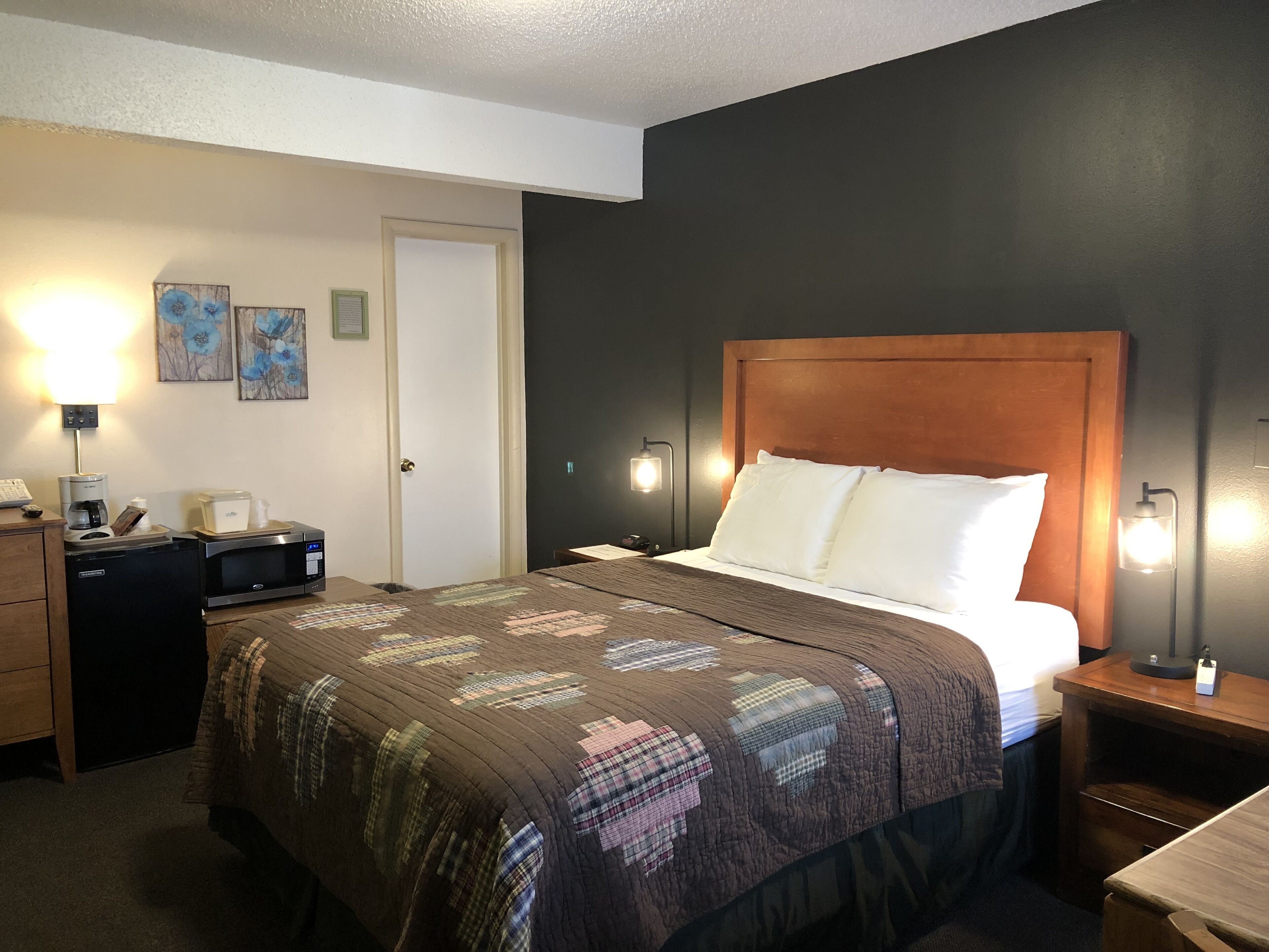 A hotel room with a bed, bedside lamps, a desk with a lamp, a coffee maker, and a microwave.