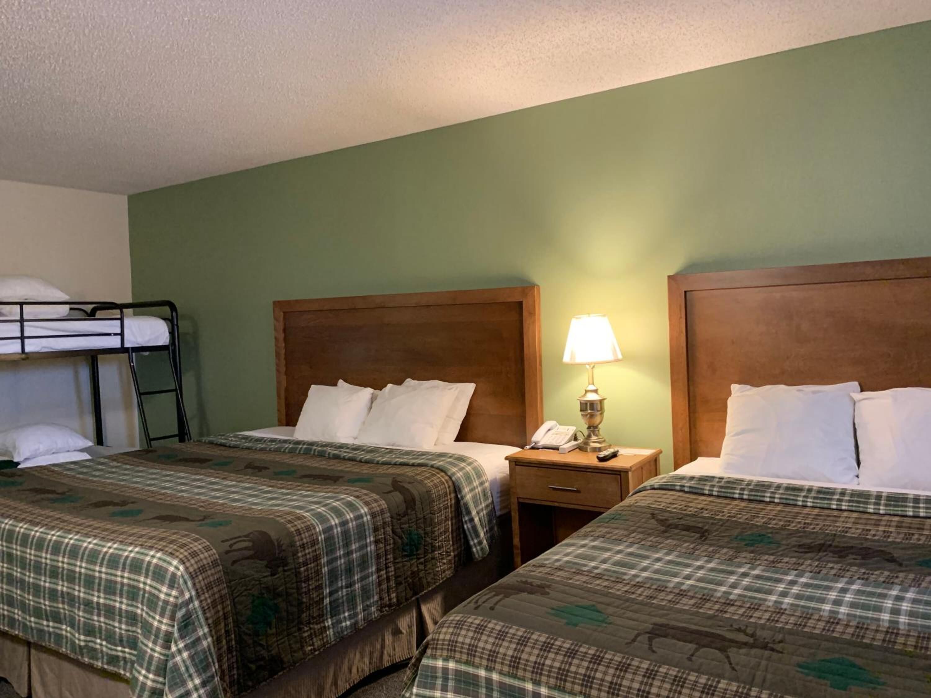 A hotel room with two beds, each with a wooden headboard and plaid bedding. There is a nightstand with a lamp and a phone between the beds.