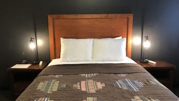 Un lit avec une couette marron, des oreillers blancs et une tête de lit en bois. Il y a deux tables de chevet avec des lampes et une petite carte sur chacune.