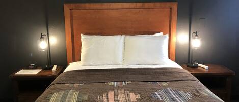Un lit avec une couette marron, des oreillers blancs et une tête de lit en bois. Il y a deux tables de chevet avec des lampes et une petite carte sur chacune.