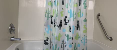 A bathroom with a bathtub, a shower curtain with cactus patterns, a grab bar, and a towel hanging on the wall.