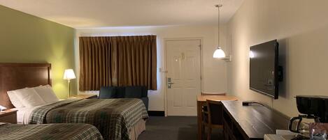 Habitación de hotel con dos camas, un escritorio, un televisor, una cafetera y una puerta.