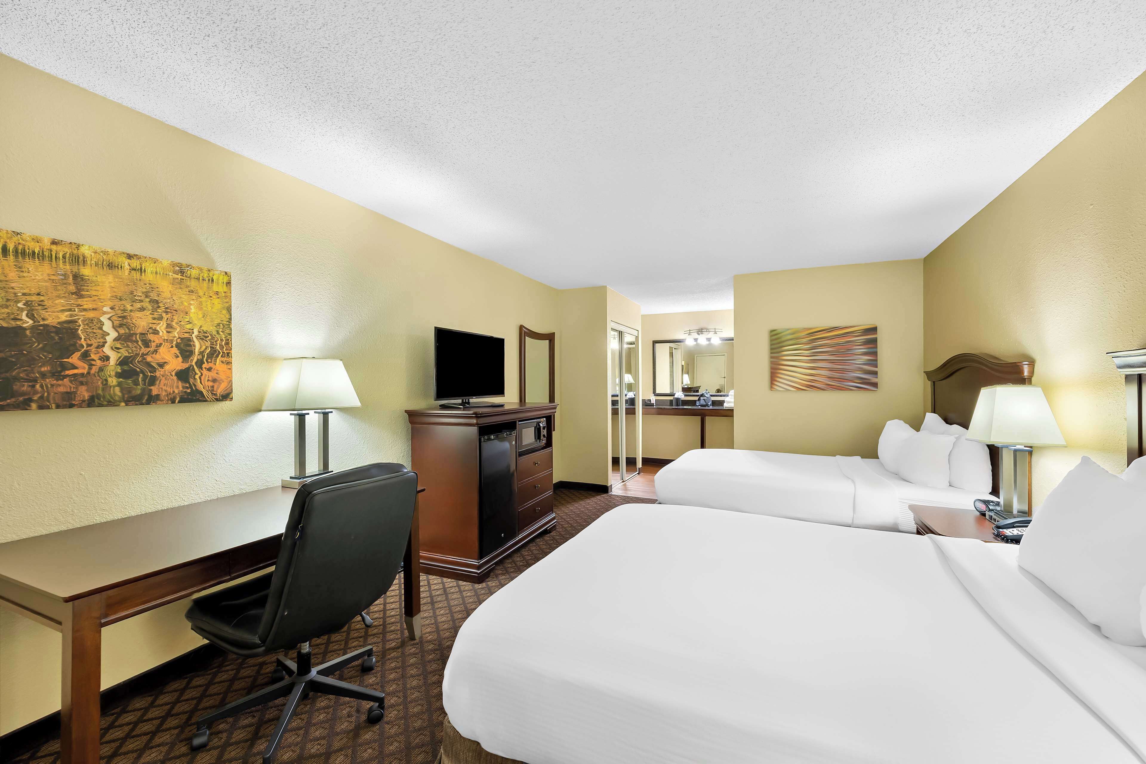 A hotel room with two beds, a desk, a chair, a television, and a desk lamp.