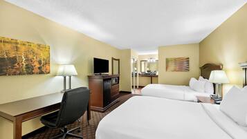 A hotel room with two beds, a desk, a chair, a television, and a desk lamp.