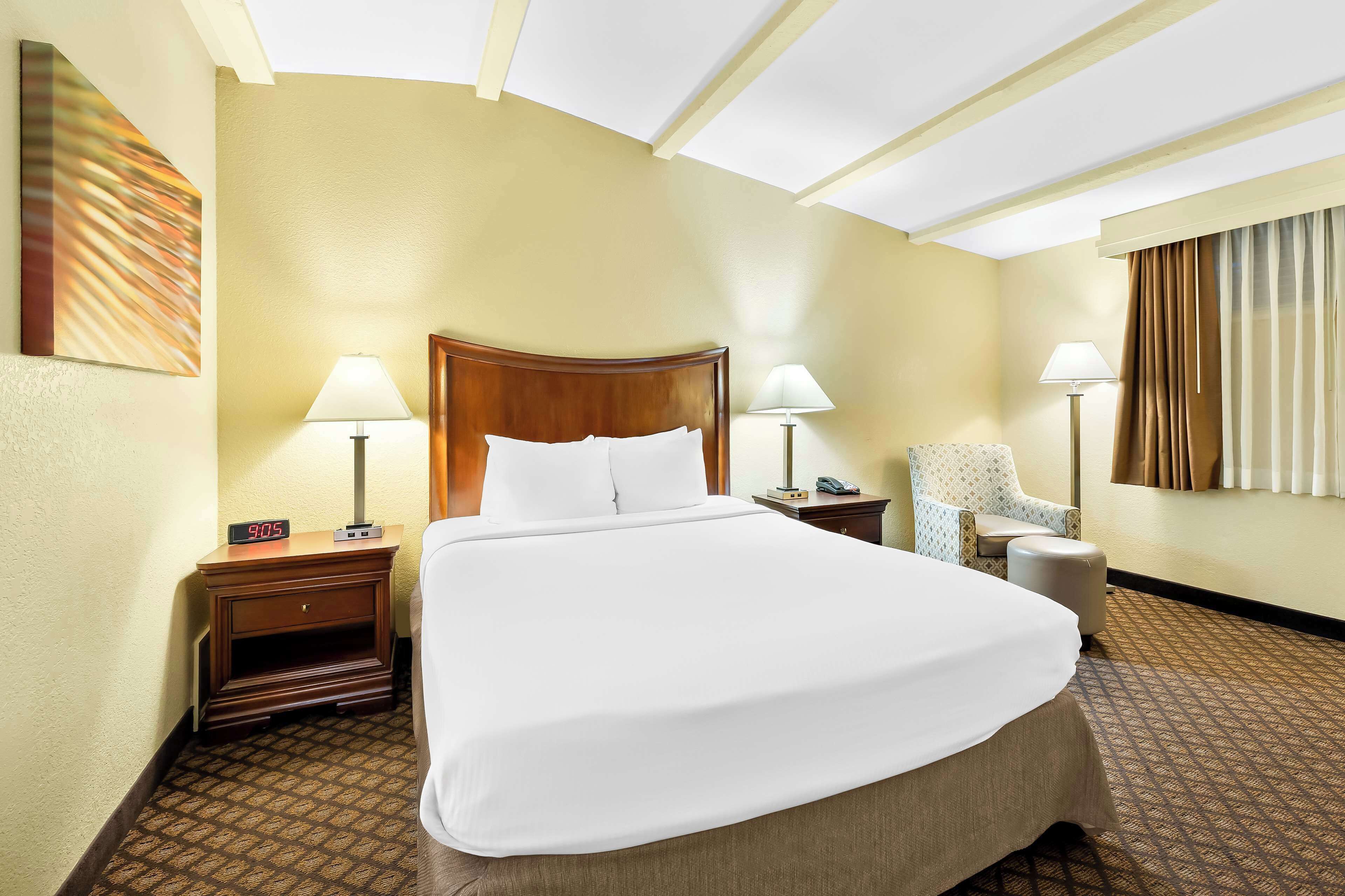 A hotel room with a large bed, two bedside tables, a chair, and a lamp.