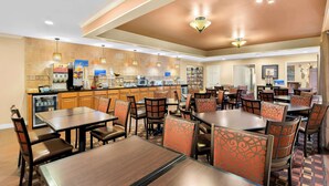 Un espace repas d’hôtel comprenant plusieurs tables et chaises, un coin cuisine et un espace dédié au café.