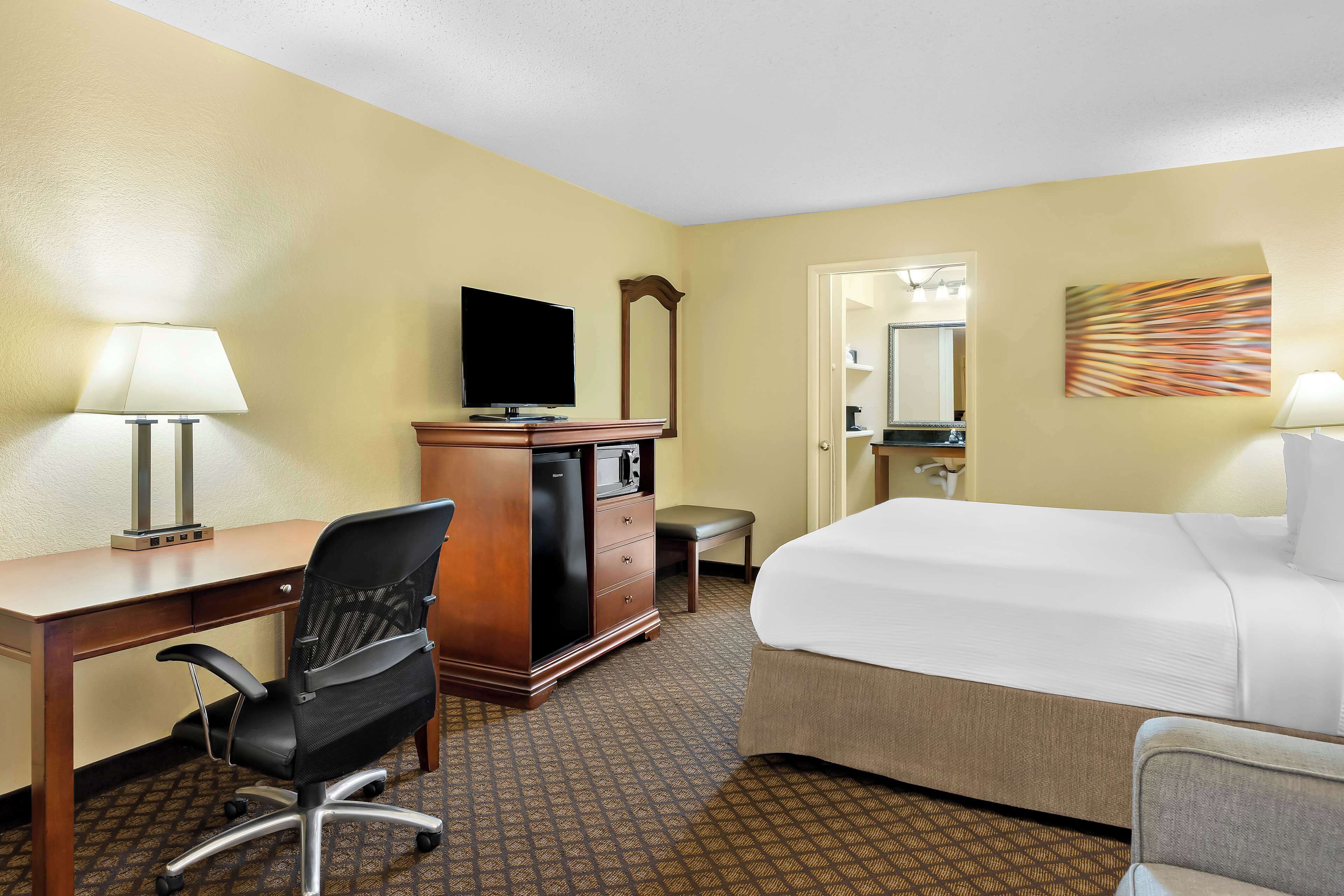 Ein Hotelzimmer mit Bett, Schreibtisch, Stuhl, Kommode, Fernseher und Spiegel.