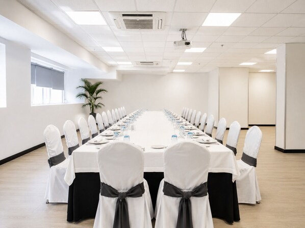 A conference room with a long table, chairs with white covers and black sashes, and a potted plant. - Hotel Chamartin The One (Madrid)