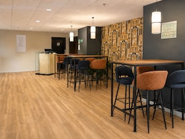 Zona de bar moderna con taburetes altos, una mesa de madera y un revestimiento de pared con diseño.
