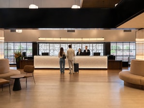 A reception area with a reception desk, seating, and large windows. - Hotel Chamartin The One (Madrid)