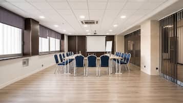 Un salón de conferencias con una larga mesa, sillas, una pantalla para proyector y una pizarra.