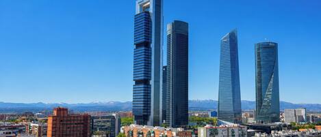 Un paisaje urbano con rascacielos modernos, un cielo azul despejado y montañas distantes.
