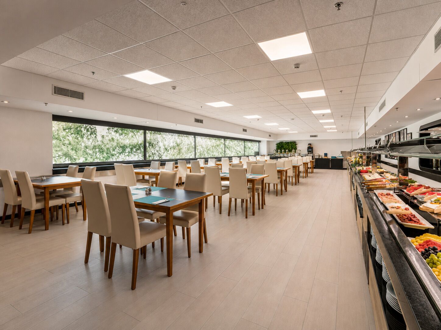 Un'ampia mensa con numerosi tavoli e sedie, un'area buffet con diverse opzioni gastronomiche e grandi finestre che offrono luce naturale.