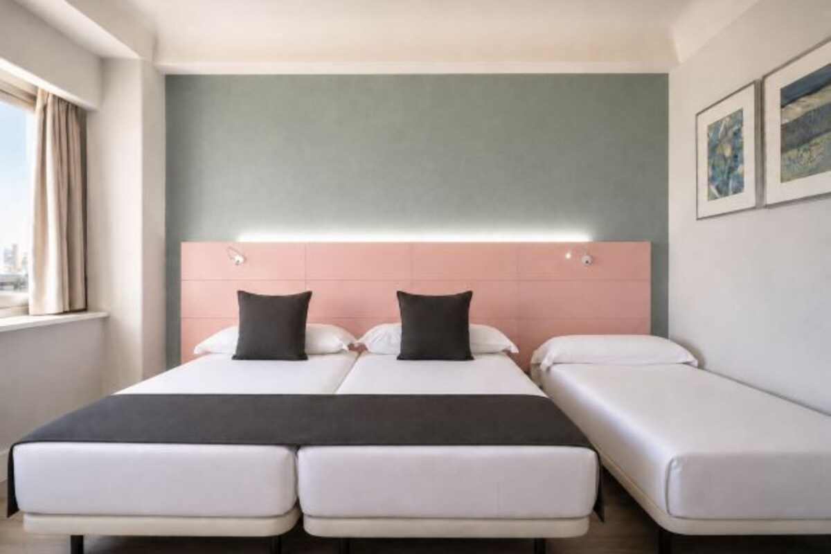 A hotel room with a bed, a bedside table, and a window.