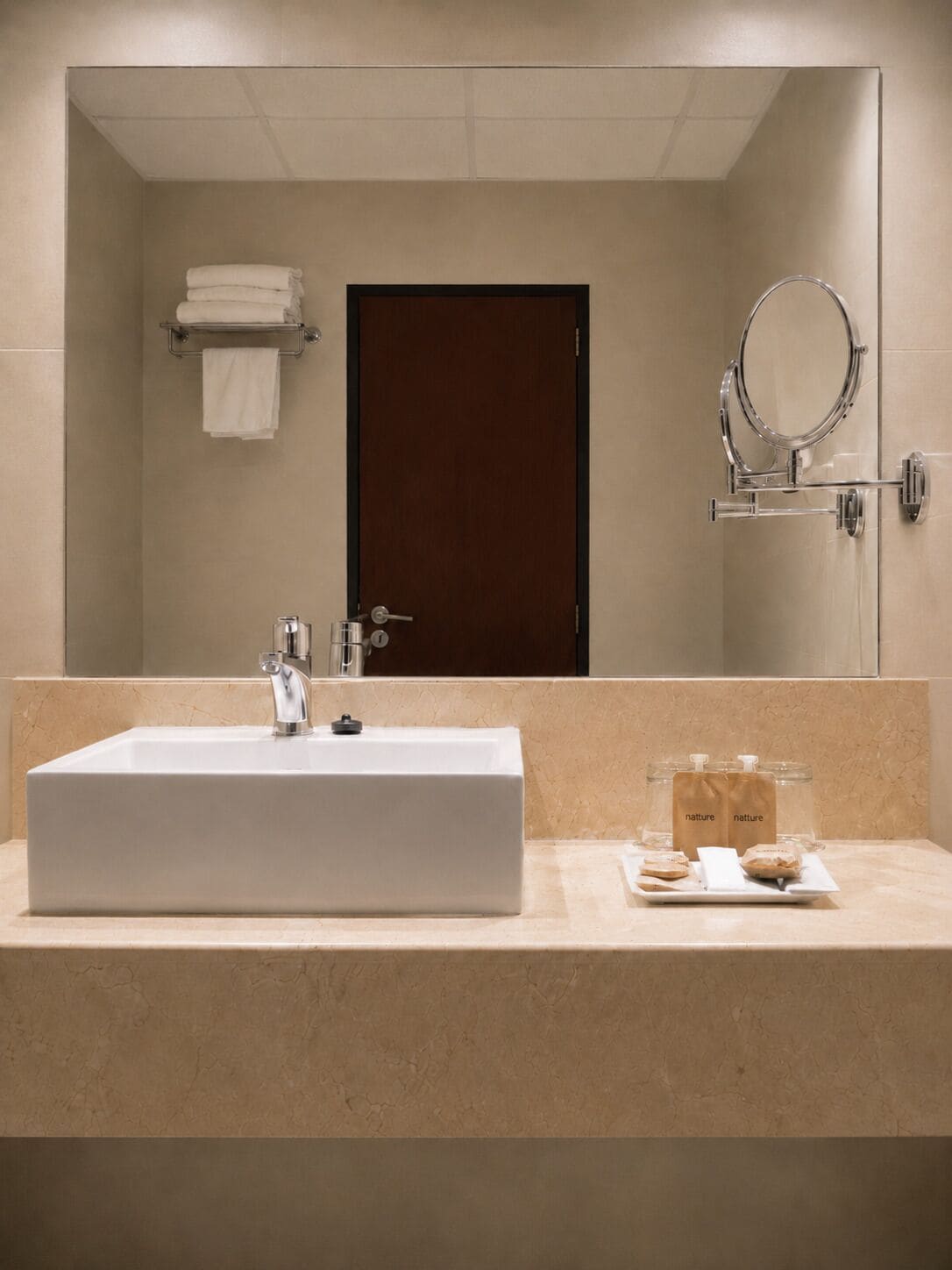 A bathroom with a large rectangular sink, a mirror, a towel rack, and a door.