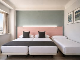 Una camera d'albergo con un letto matrimoniale, un letto singolo e vista sulla città.