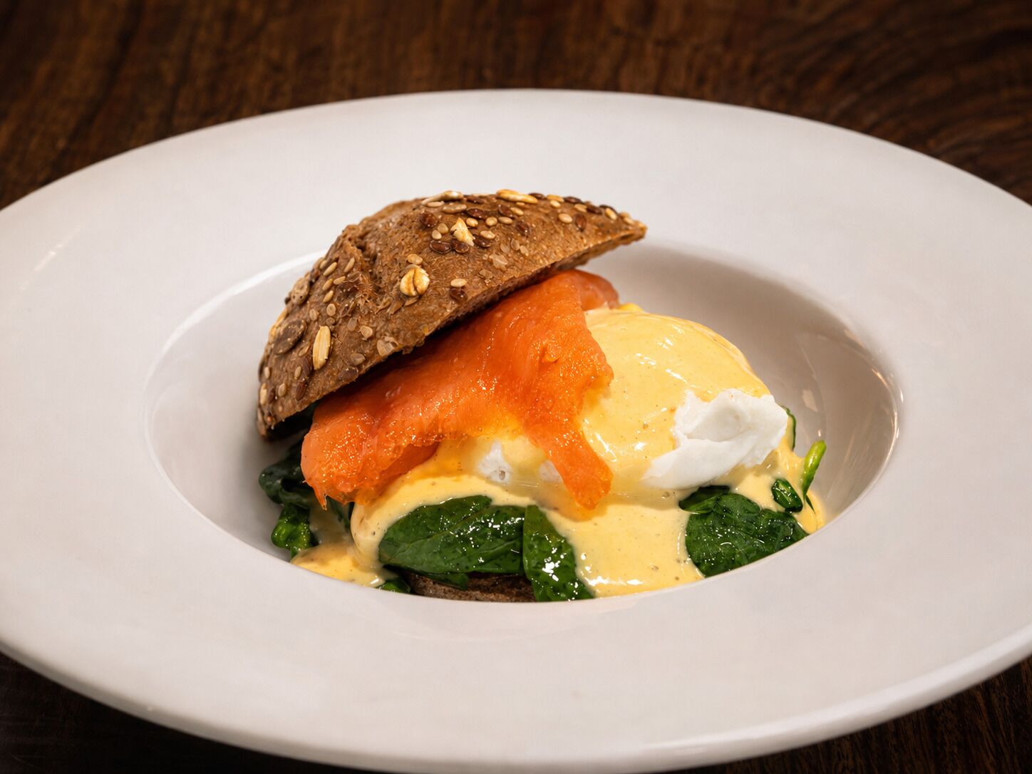 A plate with a sandwich, spinach, and a poached egg with hollandaise sauce.