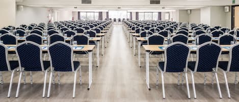 A conference room with rows of tables and chairs, equipped with water bottles and papers.