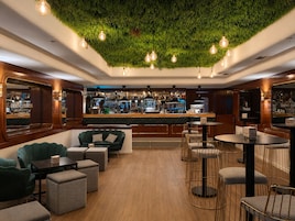 A bar area with a green wall, wooden bar counter, and seating with round tables and chairs.