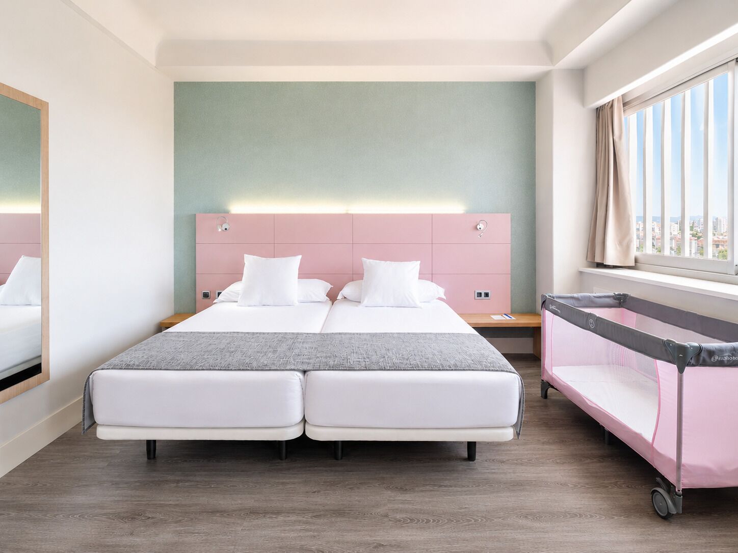 A double bed with a headboard, a bedside table, a window with curtains, and a crib with a canopy.
