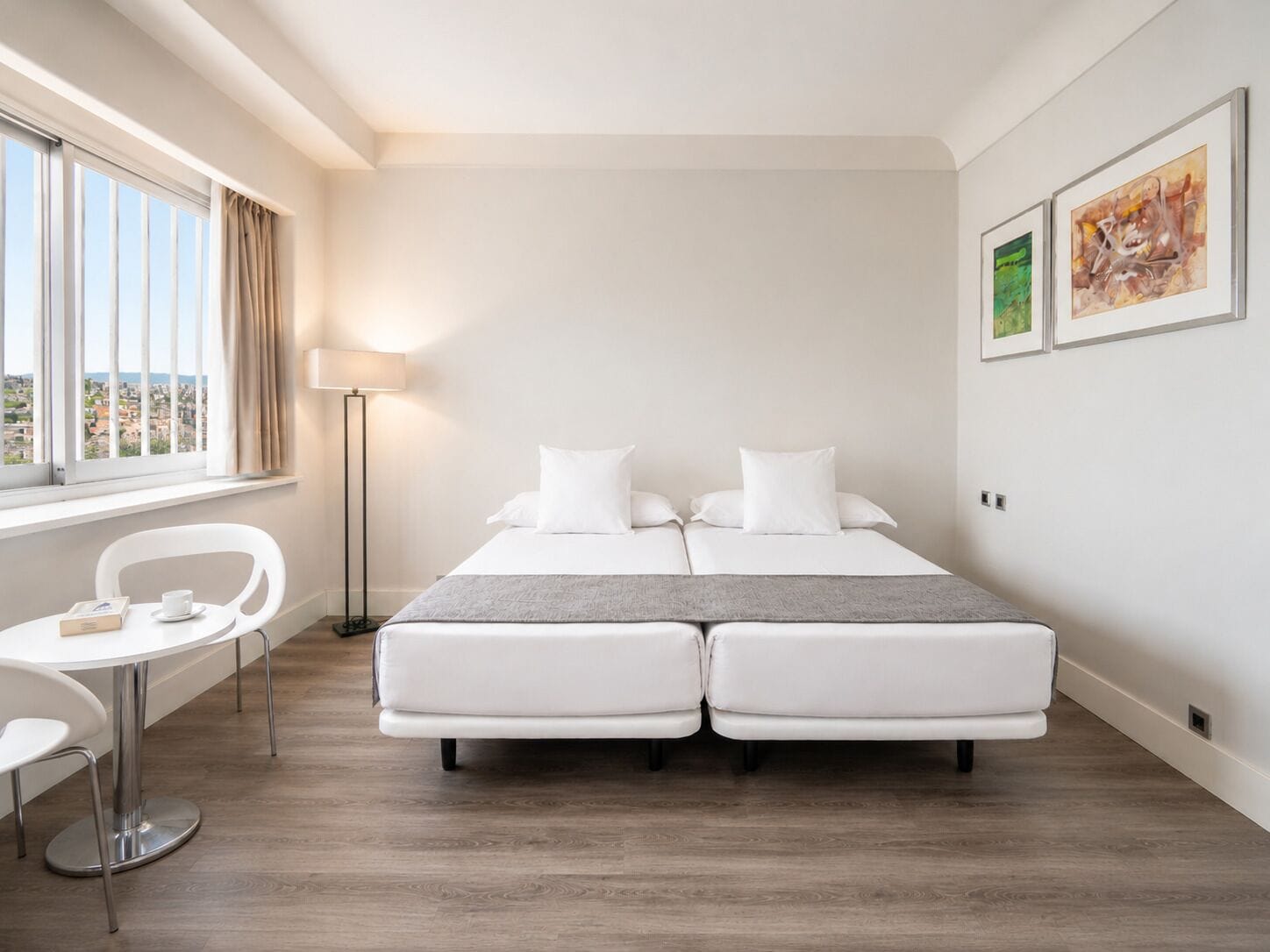Una camera d'albergo con un letto, una scrivania, una sedia, una lampada e opere d'arte alle pareti.