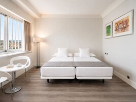 Ein Hotelzimmer mit Bett, Schreibtisch, Stuhl, Lampe und einem Kunstwerk an der Wand.