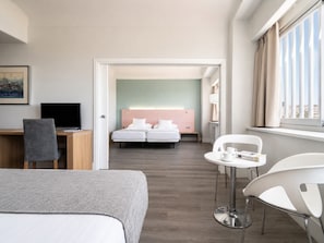 A hotel room with a bed, a desk with a computer, a chair, a small table with a cup and book, and a window with curtains. - Hotel Chamartin The One (Madrid)