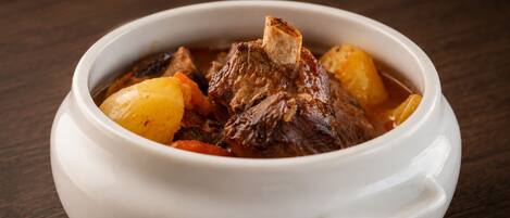 A white ceramic bowl containing a stew with meat and potatoes.