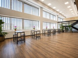 Tilava sisätila, jossa on useita pöytiä ja tuoleja, suuret ikkunat, joissa on sälekaihtimet, sekä ruukkukasveja.