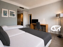 Ein Hotelzimmer mit zwei Betten, einem Schreibtisch mit Computer, einem Sessel, einem Fernseher und Bildern an der Wand.