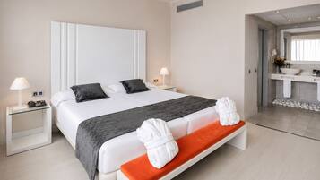 Habitación de hotel con una cama grande, mesitas de noche, un banco y un baño visible a través de una puerta abierta.