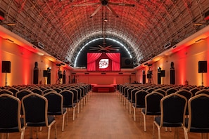 An auditorium with rows of chairs, a stage with a red curtain, and a large screen displaying 'The ONE'. - Hotel Chamartin The One (Madrid)