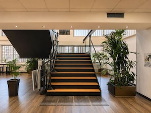 A modern staircase with wooden steps and metal railings, flanked by potted plants and a view of the outside. - Hotel Chamartin The One (Madrid)