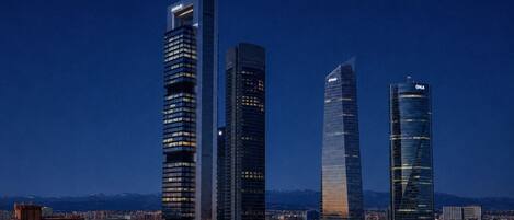 A cityscape with modern high-rise buildings, including a distinctive curved skyscraper and a tall rectangular building with illuminated signage.